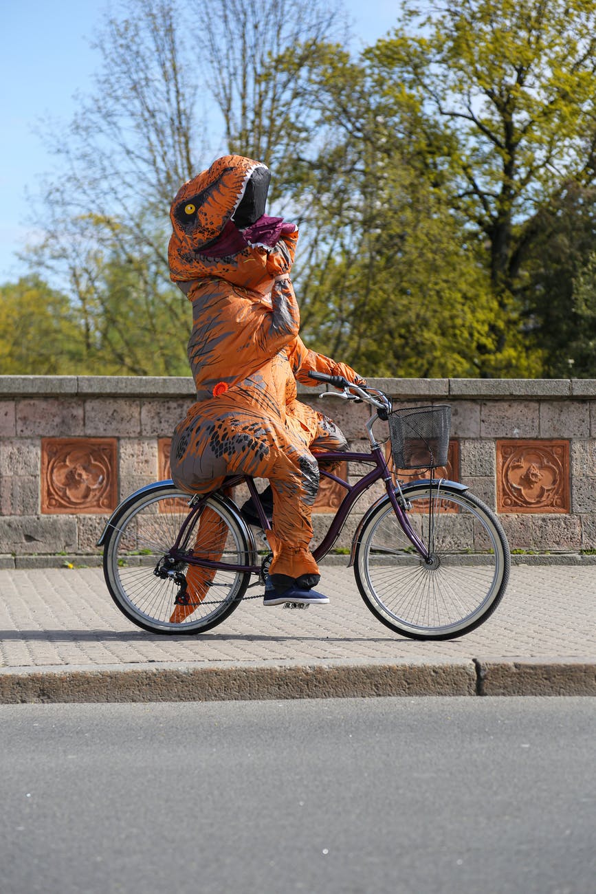 unrecognizable performer in costume of dinosaur riding bicycle