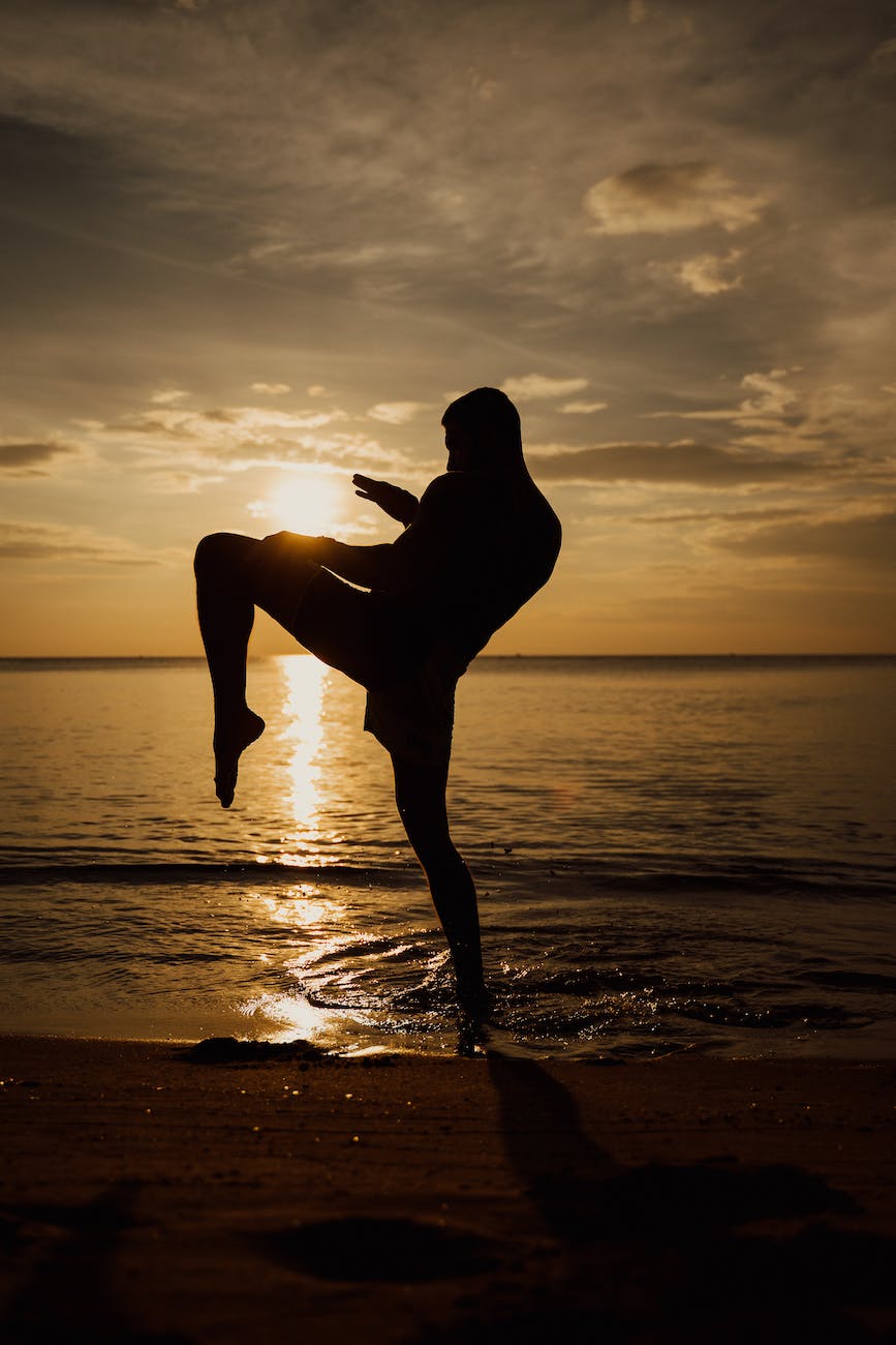 silhouette of man practicing kickboxing on the seashore during sunset