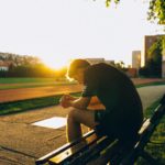 man sitting on bench near track field while sun is setting