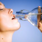 woman drinking water from glass bottle