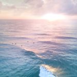 unrecognizable tourists swimming in wavy ocean at sundown